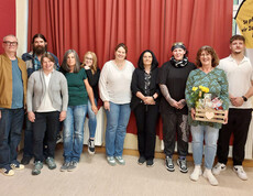 Gruppenfoto von mehreren Personen in einem Raum im Hintergrund ein roter Vorhang.