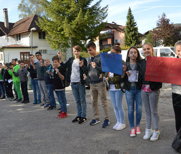 Viele Kinder stehen hinter einem Zaun im Freien.