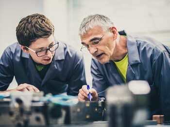 Senior engineer explaining machine functioning to his student Senior engineer explaining machine functioning to his student
