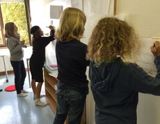 Kinder schreiben gemeinsam Begriffe und Ideen auf große Papierbögen an der Wand und erarbeiten Regeln für das Miteinander im Unterricht.