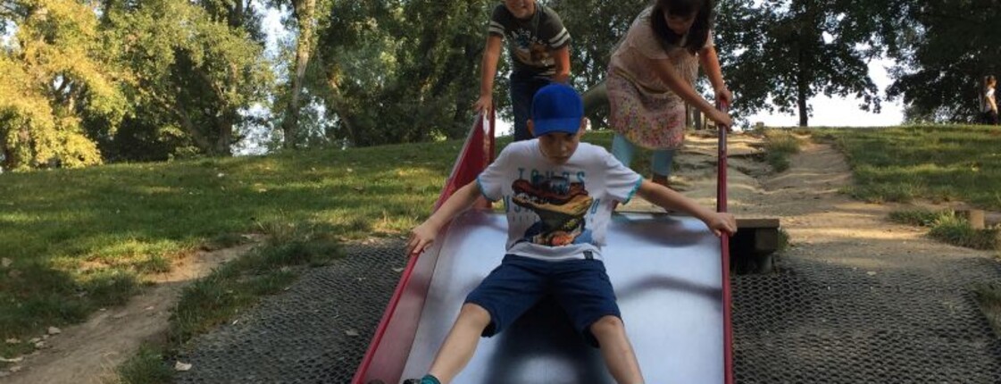 Kinder nutzen eine breite Rutsche auf einem Spielplatz im Donaupark und verbringen gemeinsam Zeit im Freien.