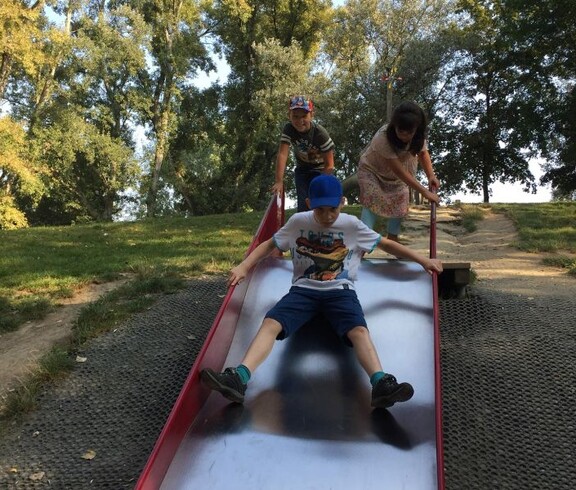Kinder nutzen eine breite Rutsche auf einem Spielplatz im Donaupark und verbringen gemeinsam Zeit im Freien.