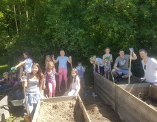 Kinder und Begleitpersonen befüllen gemeinsam Hochbeete mit Erde und bereiten die Pflanzflächen für Gartenprojekte vor.