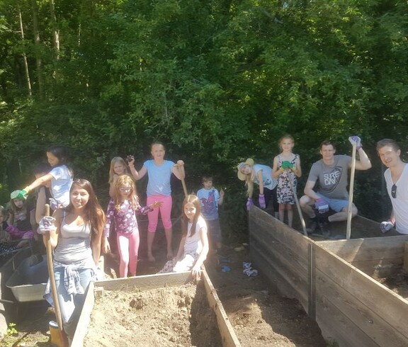 Kinder und Begleitpersonen befüllen gemeinsam Hochbeete mit Erde und bereiten die Pflanzflächen für Gartenprojekte vor.