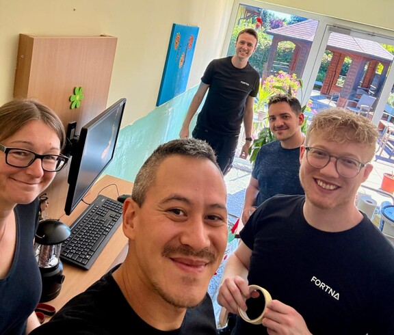 Das Team von Fortna lächelt in die Kamera. Im Hintergrund ist die abgeklebte Wand im Aufenthaltsraum des Pflegewohnhauses zu sehen.