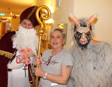 Nikolaus und Krampus posieren vor der Kamera, in der Mitte steht eine Pflegerin und hält den Stab des Nikolaus.