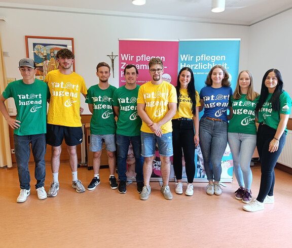 Zehn junge Erwachsene der Landjugend stehen mit bunten T-Shirts vor Caritas-Infobannern