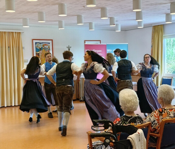 Junge Tänzer*innen in Tracht führen traditionellen Volkstanz vor älteren Menschen auf
