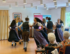 Junge Tänzer*innen in Tracht führen traditionellen Volkstanz vor älteren Menschen auf