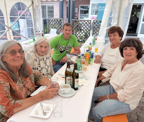 Gäste sitzen gemeinsam an einem Tisch im Festzelt und genießen Speisen und Getränke beim Sommerfest.