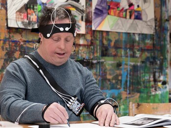 Mann in einem Künstleratelier beim Zeichnen umgeben von einer technischen Ausrüstung.