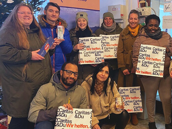 Eine Gruppe Erwachsener steht nebeneinander und hält Caritas Säcke in der Hand. Links ist ein Christbaum zu sehen.