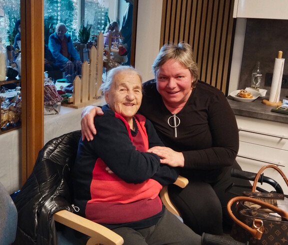 Zwei Personen sitzen eng beieinander, festliche Deko und weitere Gäste im Hintergrund