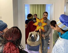 Familie öffnet drei Kindern, die als Sternsinger unterwegs sind, die Tür.