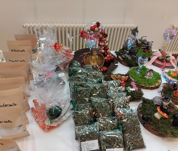 Verschiedene handgefertigte Produkte wie Kräutersalz, getrocknete Kräuter und dekorative Dioramen auf einem Tisch ausgestellt.