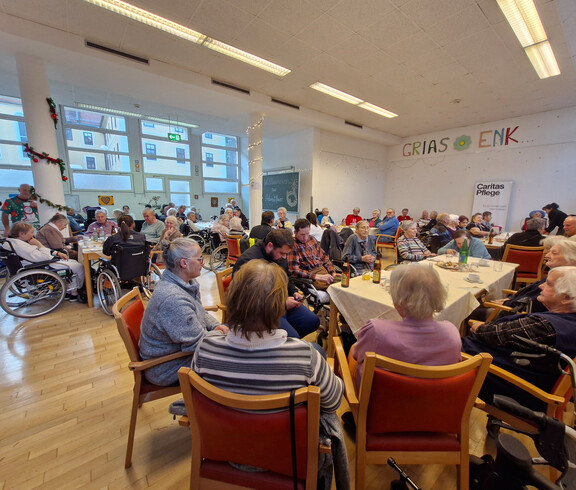 Viele Gäste sitzen an Tischen, Raum mit Weihnachtsdeko und Schriftzug „GRIAS ENK“
