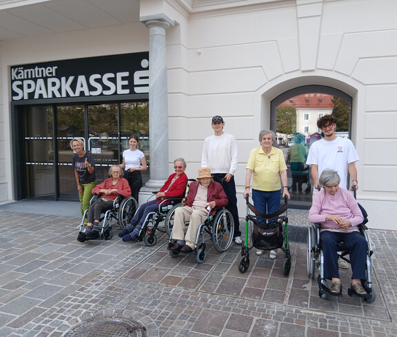 Gruppe von Senior*innen mit Begleitpersonen posiert vor dem Eingang der Kärntner Sparkasse.