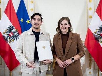 Ein junger Mann nimmt eine Auszeichnung entgegen, im Hintergrund sind Österreich Fahnen.