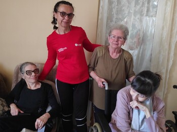 Gruppenfoto: Eine Caritas-Mitarbeiterin in der Mitte mit rotem Caritas-Shirt - daneben eine ältere Dame. Links und rechts zwei jüngere Frauen, die sitzen. Alle lächeln in die Kamera.