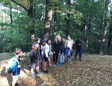 Kinder stehen gemeinsam auf einer Lichtung im Wald und nehmen an einer Natur- und Teamaktivität mit spielerischen Aufgaben teil.