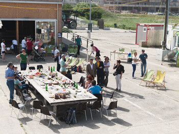 Auf einem Bereich des ehemaligen Flugfelds Aspern steht ein großer, gedeckter Tisch, der ist umringt von Menschen und Liegestühlen.  