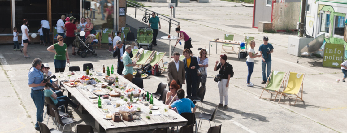 Auf einem Bereich des ehemaligen Flugfelds Aspern steht ein großer, gedeckter Tisch, der ist umringt von Menschen und Liegestühlen.  