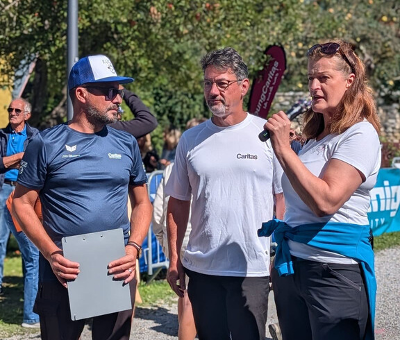 Drei Personen, darunter Caritasdirektor Ernst Sandriesser, sprechen vor dem Startbereich des Charity Runs mit Publikum im Hintergrund.