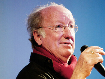 Ein Herr hält ein Mikrofon in der Hand. Er trägt einen roten Schal sowie eine Brille.