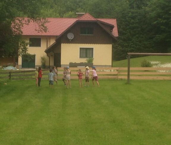 Kinder spielen gemeinsam auf einer großen Wiese vor einem Gästehaus und verbringen Zeit im Freien während einer Projektwoche.