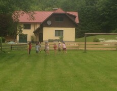 Kinder spielen gemeinsam auf einer großen Wiese vor einem Gästehaus und verbringen Zeit im Freien während einer Projektwoche.