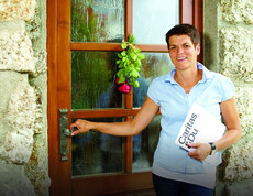 Eine Frau mittleren Alters mit kurzen schwarzen Haaren hält in der einen Hand eine Pressemappe der Caritas und in der anderen Hand eine Türklinke. 