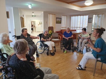 Eine Gruppe von Senior*innen sitzt im Kreis teilweise auf Stühlen, teilweise im Rollstuhl.