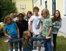Kinder stehen bei einer Teamaufgabe gemeinsam auf einer Plane im Schulgarten und fördern spielerisch Zusammenarbeit sowie Geschicklichkeit.