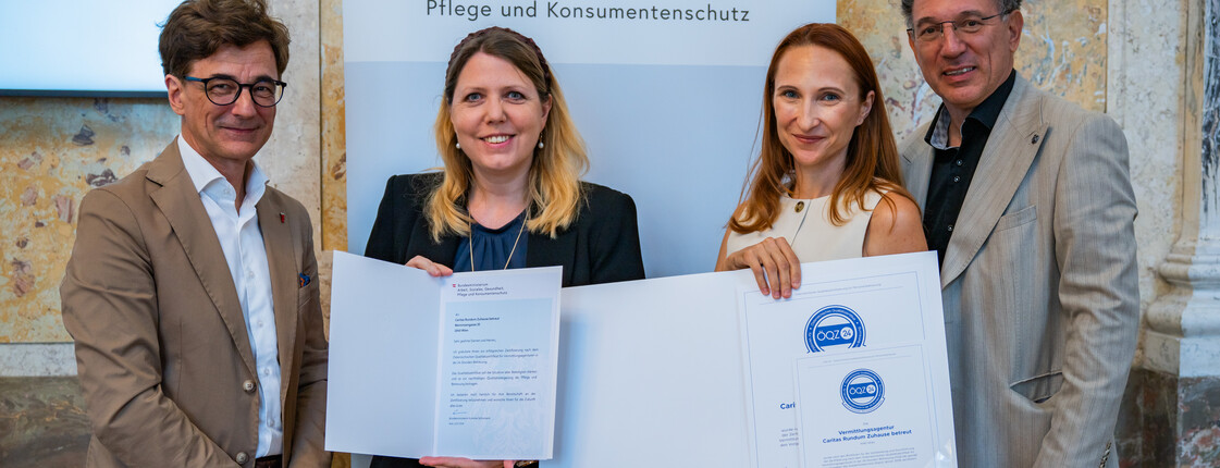 Vier Personen bei der Verleihung des Österreichischen Qualitätszertifikats ÖQZ-24 im Bundesministerium. In der Bildmitte wird die Urkunde für die Auszeichnung der Caritas Rundum Zuhause betreut im Bereich 24-Stunden-Betreuung präsentiert.