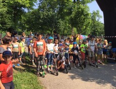 Kinder stehen mit Rollern am Start einer Sportveranstaltung im Freien und bereiten sich gemeinsam auf einen Wettbewerb vor.