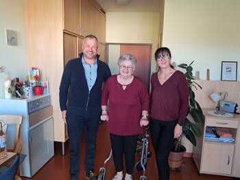 Bürgermeister Herr Tulnik und Pflegedienstleitung Frau Simko stehen gemeinsam mit Frau Krammer in ihrem Zimmer. Alle drei lächeln in die Kamera anlässlich ihres 90. Geburtstags.