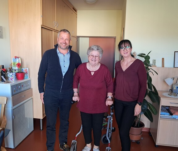 Bürgermeister Herr Tulnik und Pflegedienstleitung Frau Simko stehen gemeinsam mit Frau Krammer in ihrem Zimmer. Alle drei lächeln in die Kamera anlässlich ihres 90. Geburtstags.