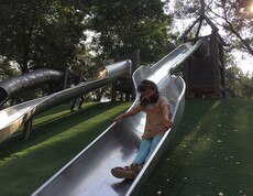 Ein Kind rutscht eine große Metallrutsche hinunter, während weitere Kinder auf dem Spielplatz im Donaupark spielen.