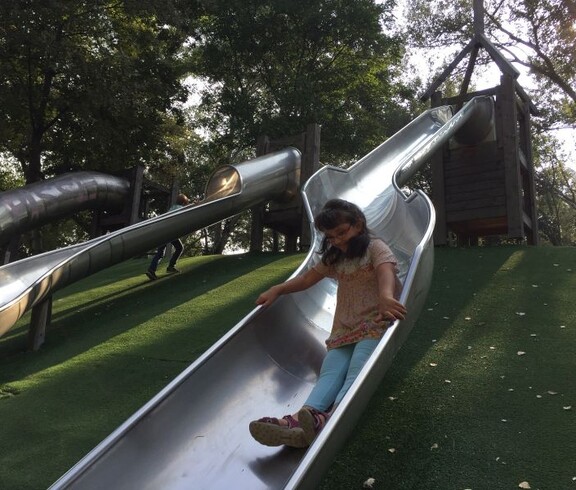 Ein Kind rutscht eine große Metallrutsche hinunter, während weitere Kinder auf dem Spielplatz im Donaupark spielen.