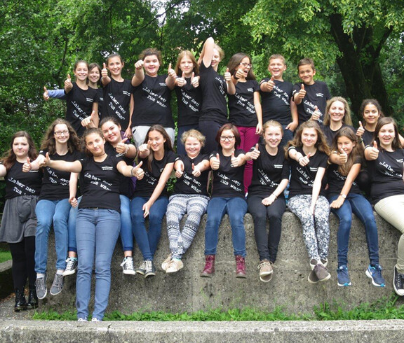 Die Gruppe der Jugendbotschafter sitzen auf einem hohen Stein und zeigen mit dem Daumen in die Höhe. Sie tragen alle ein schwarzes Tshirt mit der Aufschrift: "Laber ned tua was." 