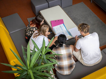 Vier Schüler*innen sitzen auf der Couch im Gemeinschaftsraum und sehen gemeinsam in ihre Schulunterlagen.