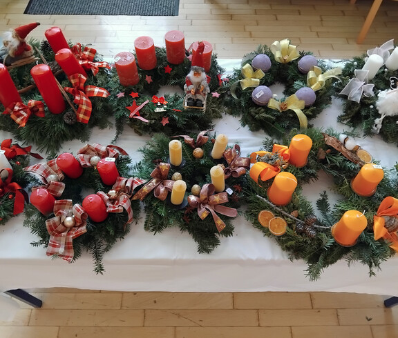 Verschiedene dekorative Weihnachtskränze mit Kerzen und festlichen Verzierungen auf einem Tisch arrangiert.