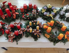 Verschiedene dekorative Weihnachtskränze mit Kerzen und festlichen Verzierungen auf einem Tisch arrangiert.