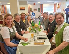 Im Gemeinschaftsraum sitzen die Gäste an einem gedeckten Tisch. Unter ihnen befinden sich Bürgermeister Josef Niggas, Caritaspräsidentin und -direktorin Nora Tödtling-Musenbichler sowie Max Tödtling, Moderator der Feier und ehemaliger Hausleiter. Im Hintergrund sind weitere Tische und der Raum sichtbar.