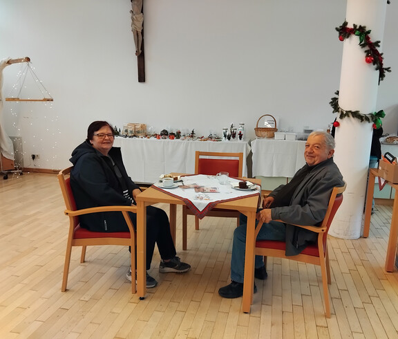 Zwei ältere Personen sitzen an einem Tisch im Speisesaal und genießen Essen und Getränke. 