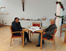 Zwei ältere Personen sitzen an einem Tisch im Speisesaal und genießen Essen und Getränke. 