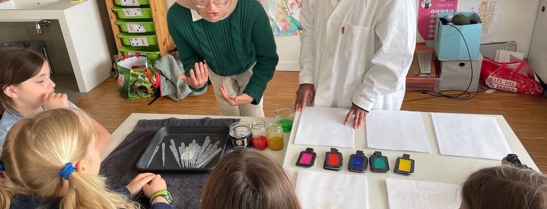 Kinder verfolgen einen naturwissenschaftlichen Workshop mit Farbexperimenten. Materialien und Demonstrationen machen chemische Prozesse anschaulich.