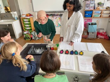 Kinder verfolgen einen naturwissenschaftlichen Workshop mit Farbexperimenten. Materialien und Demonstrationen machen chemische Prozesse anschaulich.