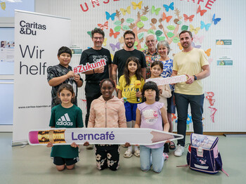 Gruppe aus Kindern und Erwachsenen im Lerncafé mit Schildern zu #Zukunft und #Chancen bei der Antenne-Schulstartaktion.