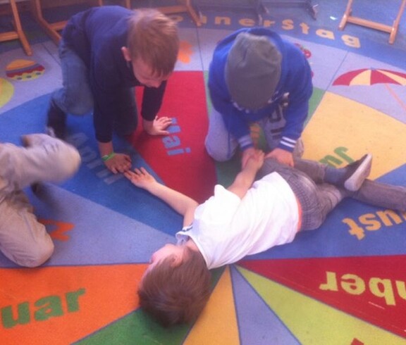 Kinder üben gemeinsam Erste-Hilfe-Maßnahmen auf einem Teppich und lernen spielerisch grundlegende Kenntnisse zur Hilfeleistung.